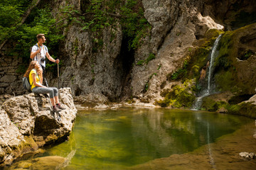 Fototapeta na wymiar active young couole hiking in nature resting near waterfalll and taking pictures with camera