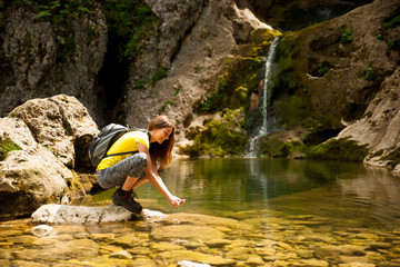 active young woman drinking water from a mountain creek on a warm spring day - obrazy, fototapety, plakaty