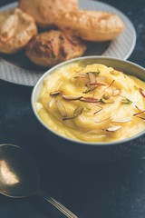 Shrikhand with fried Puri / Poori served in a bowl and plate over moody background. Selective focus