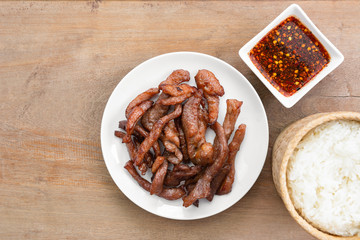 top view of fried sun dried pork in a ceramic dish served with spicy sauce and sticky rice on wooden table. thai style delicious food menu.