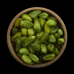 shelled green pistachio in wooden cup isolated on black background. top view