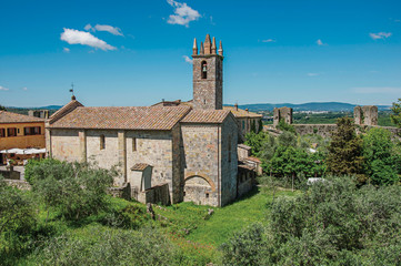 Fototapeta na wymiar Overview of church and bell tower with trees around in the hamlet of Monteriggioni. A medieval fortress, surrounded by stone walls, at the top of a hill, near Siena. Located in the Tuscany region 