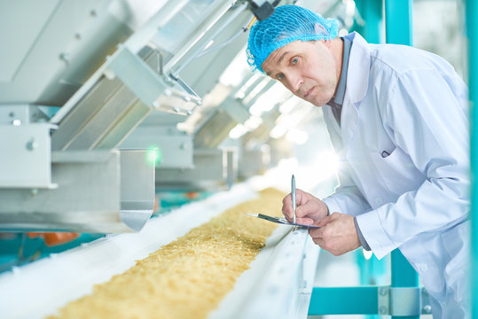 Waist up portrait  of  senior factory worker doing  production quality inspection in food industry holding clipboard and making notes standing by conveyor belt, copy space