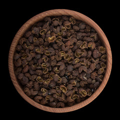 Sichuan pepper in wooden cup isolated on black. top view