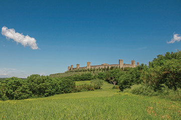 Fototapeta na wymiar View of the stone walls of the hamlet of Monteriggioni on top of hill and surrounded by trees. A medieval fortress, surrounded by walls at the top of a hill near Siena. Located in the Tuscany region 