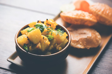 Chatpate Masala Aloo Sabzi fry OR Bombay potatoes served with fried puri or Indian bread made up of wheat in a plate, selective focus