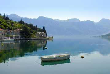 Fototapeta premium Boat on still water against mountain ridge and ancient city. Bay of Kotor, Montenegro