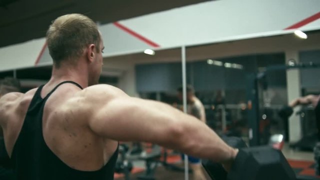 Bodybuilder in gym doing Lateral Raise, shallow depth of field. Slow motion