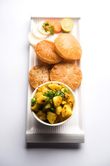 Chatpate Masala Aloo Sabzi fry OR Bombay potatoes served with fried puri or Indian bread made up of wheat in a plate, selective focus