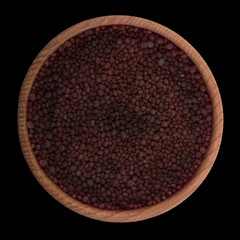seeds of black mustrand in wooden cup isolated on black. top view