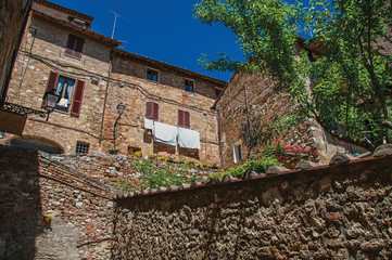 Fototapeta na wymiar View of stone wall, old buildings with flowering plants and blue sky at Colle di Val d Elsa. A village with its historic center preserved and known by its crystal production. In the Tuscany region 