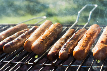 Spicy sausages grilling on portable barbecue on summer picnic. Outdoors. Smoke and fire. Close up.