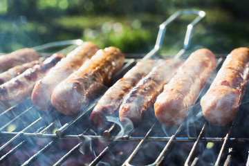 Tasty sausages grilling on portable barbecue on summer picnic. Outdoors. Smoke and fire. Close up.
