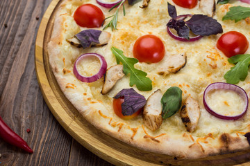 Italian Pizza with chicken, cherry tomatoes, cheese and onions on the board decorated with leaves of arugula and basil