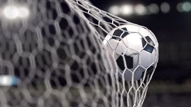 A Soccer ball flies into the net on a stadium with spot lights. The movement at the beginning is accelerated then slowly