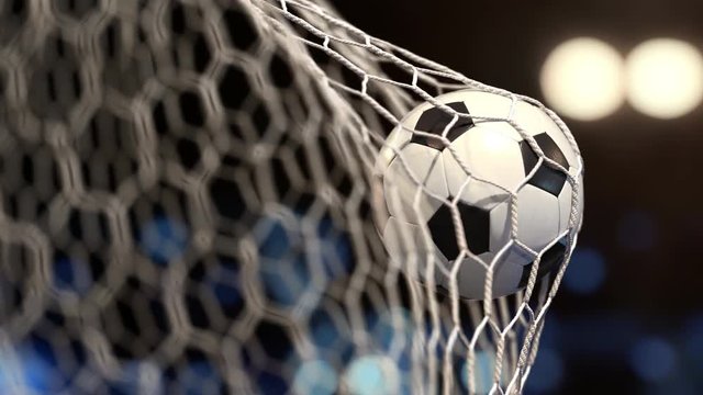 Soccer ball flies into the net on a stadium with yellow and blue lights. The movement at the beginning is accelerated then slowly
