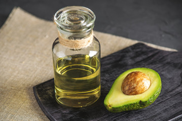 Avocado fruit and oil in glass bottle on dark background. Concept organic eco products for food and cosmetic procedures