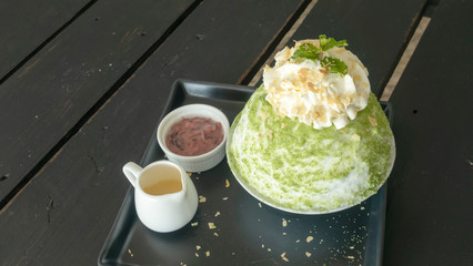 Green tea and red bean Bingsu on a wooden table.