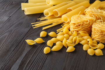 Composition of uncooked italian pasta. Spaghetti, farfalle, fusilli on dark wooden background