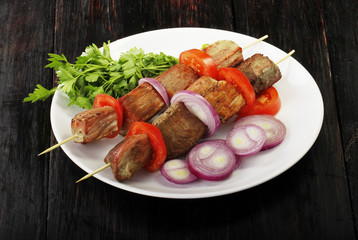 shish kebab with vegetables in plate on wooden background