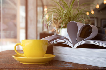 Yellow coffee cup placing together with magazine like Heart Shape under sun light flare