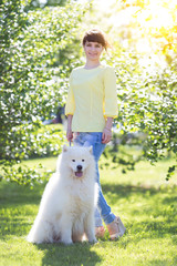 The brunette girl with a big white dog. Beautiful young girl is walking with her dog in a summer park.