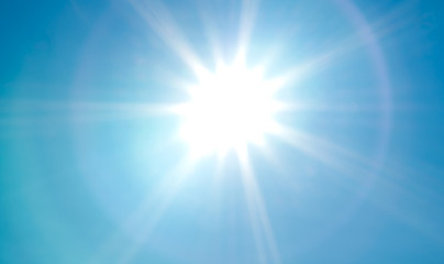 Looking up at bright, vivid sun with sunbeams and lens flare on blue summer sky