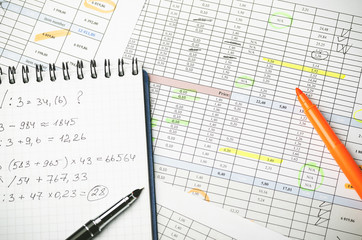 Financial tables on paper and notebook with calculations, pen and highlighter