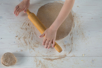 child hands rolling out dough for pizza, on a wooden table with flour