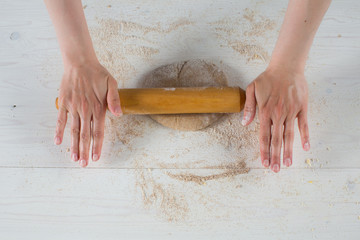 child hands rolling out dough for pizza, on a wooden table with flour