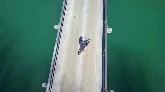 A man rides his bike on the bridge and he is riding the bicycle from one side of the bridge to another. Aerial shot.