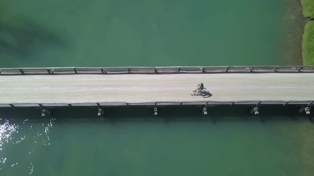 A young man is cycling across the bridge and he is really taking his time. Aerial shot.