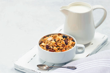 Cup of muesli with tropical fruits and white milk jug on wooden board. Concept of healthy eating in pure tones.