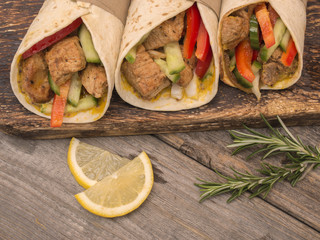 Fresh tortilla wraps with pork meat and fresh vegetables on wooden board. 