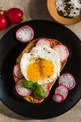 Delicious sandwich with fried eggs and radish on a black plate