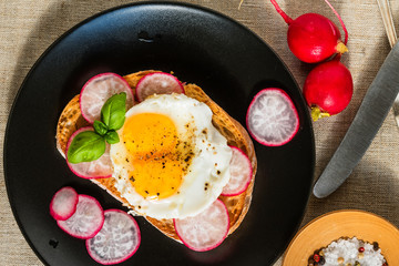 Delicious sandwich with fried eggs and radish on a black plate