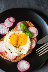Healthy organic sandwich with fried eggs, radish and basil and spices on a black background