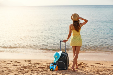 Beautiful young woman with a hat standing with suitcase on the wonderful sea background, concept of...