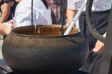 Cook with a black apron stirring an old metal pot