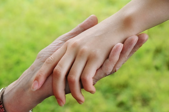 senior's hand holds the hand of a young woman, aid concept, green background