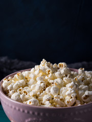 Popcorn in pink bowl on wooden board on dark background