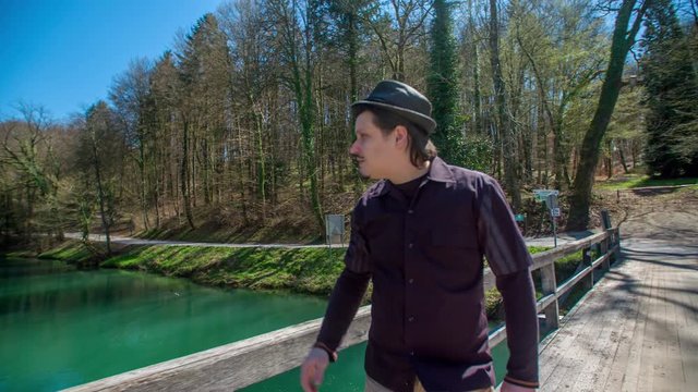 A man stops by the fence on the bridge and then he continues walking across the bridge.