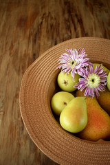 Little pears and flowers in a thatch hat against the wooden background. Top view