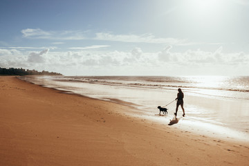 Woman walking with dog on beach at sunrise