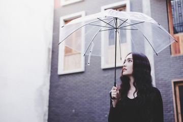 Portrait charming beautiful woman. Attractive beautiful woman is looking at sky. Gorgeous girl holds umbrella because it’s nearly raining. Glamour lady is walking around the city or town. copy space