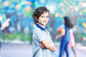 Happy young kid at school with arms crossed while schoolmates playing