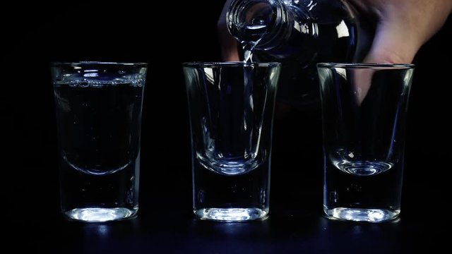  Pouring up three shots of vodka in glass against black background