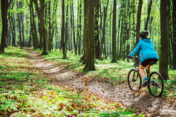 Naklejka premium young woman ride bicycle in forest by trail