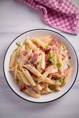 Penne pasta with bacon and sundried tomatoes. Alfredo penne pasta on white plate on wooden table. overhead, vertical