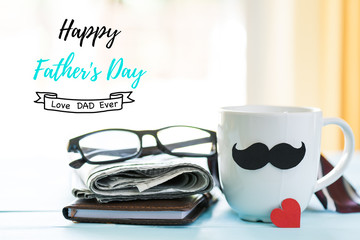 Happy fathers day concept. coffee cup with black paper mustache, red heart tag and newspaper, glasses, notebook on blue wooden table background.